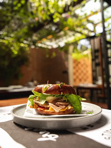 Our Smoke Ham Bagel Sandwich, pictured in our beautiful outdoor seating area. It's the perfect fuel for your day, combining smoky ham with the satisfying chew of our house-made bagel.
