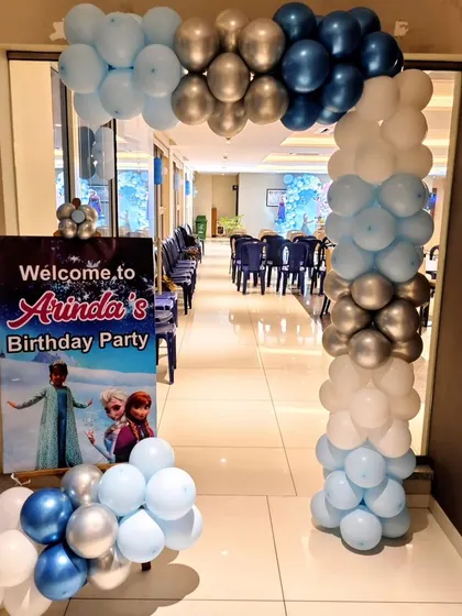 The entrance to a Frozen birthday party, with a blue, white, and silver balloon arch and a themed welcome sign.