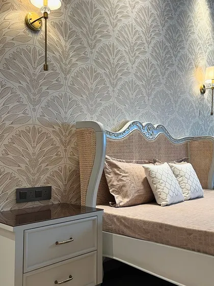A detail shot of the bed's headboard, showcasing the fine rattan work and the elegant shape of the frame. The wall-mounted lamps provide soft, focused light for reading in bed.
