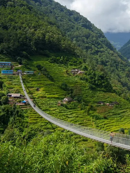 A breathtaking view of a suspension bridge stretching across a deep, green valley in the Annapurna region. These bridges are an iconic and thrilling part of the trek.