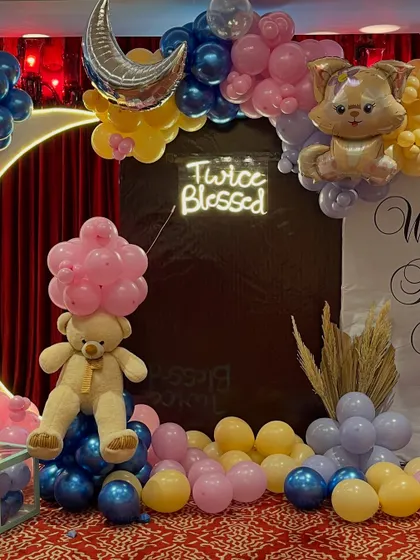 This close-up shows the "Twice Blessed" neon sign and the teddy bear prop, which is cleverly holding a cluster of pink balloons.