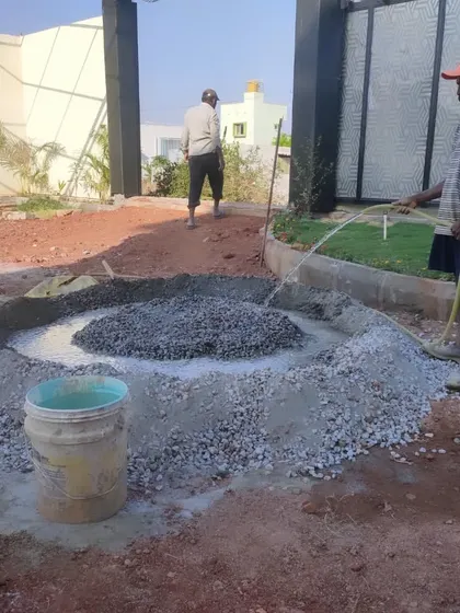 A team member watering freshly mixed concrete and gravel. This is a key step in creating a solid base for pathways or patio areas in a garden.