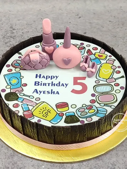 A cake for a little makeup freak. The top is decorated with edible illustrations of makeup products, with 3D fondant lipstick, nail polish, and a purse.
