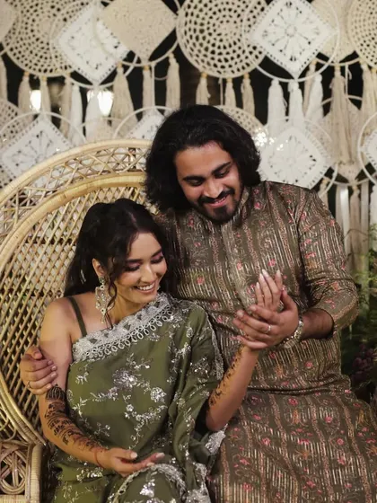 A happy couple shares a tender moment during their Mehendi night, seated on a beautiful peacock chair.