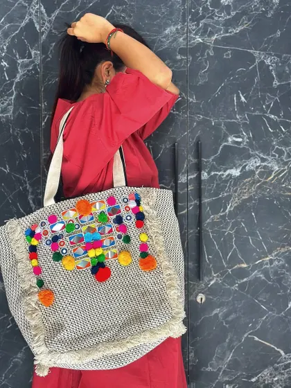 A detail shot of the vibrant, handcrafted tote bag with pom-poms and mirror work.