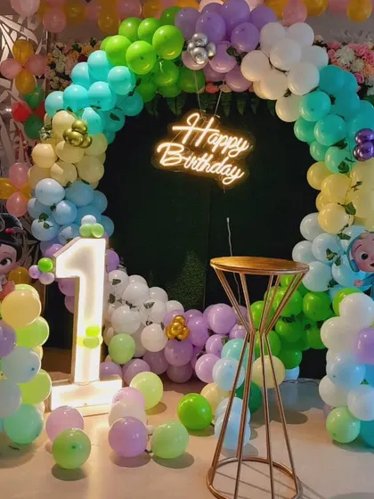 A Cocomelon first birthday party with a green artificial grass base. The decor includes a circular balloon arch and a light-up number '1'.