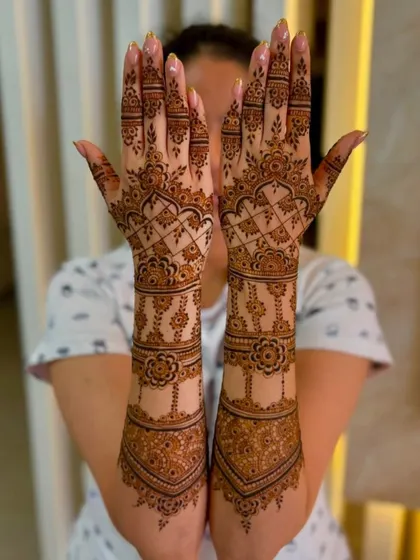 A full view of a bride holding up her hands to show the complete bridal mehandi, extending from fingertips to elbows with floral and geometric patterns.