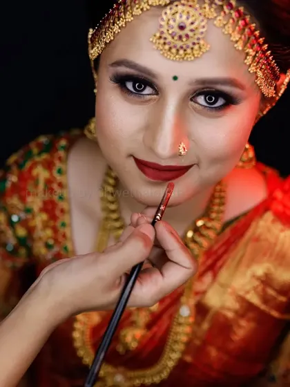 A classic muhurtham look featuring a bright red lip and defined eyes. The traditional matha patti and heavy gold jewellery are perfectly balanced with the makeup, and the bridal braid with fresh flowers is a timeless choice.