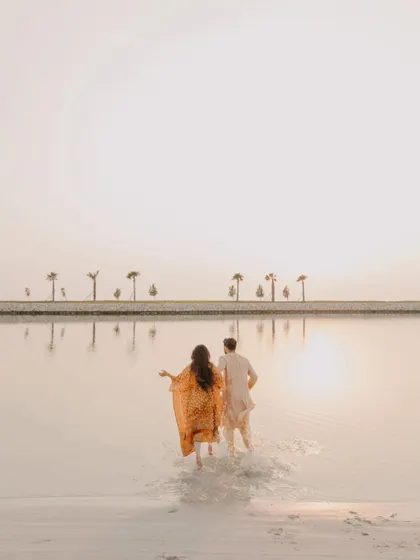 The couple walking into the water at sunset. This beautiful silhouette shot captures a serene and romantic moment from their beachside Haldi celebration in Bahrain.
