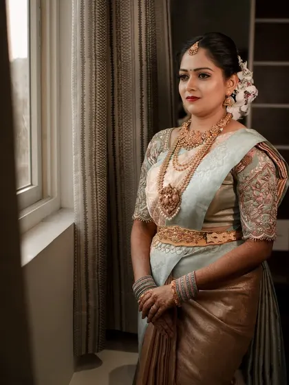 A classic bridal portrait showing a bride in her reception saree, looking thoughtfully out a window.