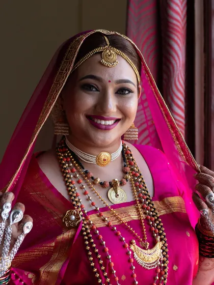 A close-up of a smiling Coorgi bride in her traditional pink muhurtham saree and veil. Her makeup is bright and joyful.