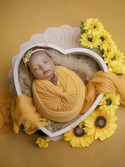A heart full of sunshine. This overhead shot shows a baby swaddled in yellow, nestled in a heart-shaped bowl and surrounded by sunflowers.