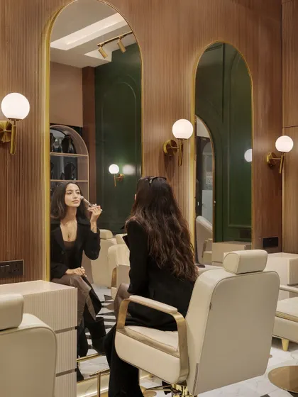 A client experience at the makeup studio. The design features arched mirrors, warm wood paneling, and globe sconces to provide perfect lighting and an opulent environment for makeup application.