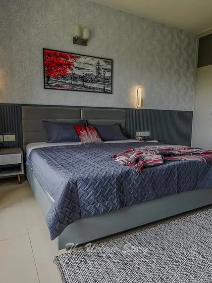 The "after" shot of a son's bedroom transformation. The room features a cool grey and blue color scheme with a textured accent wall, a comfortable upholstered bed, and modern wall sconces for a stylish, grown-up feel.