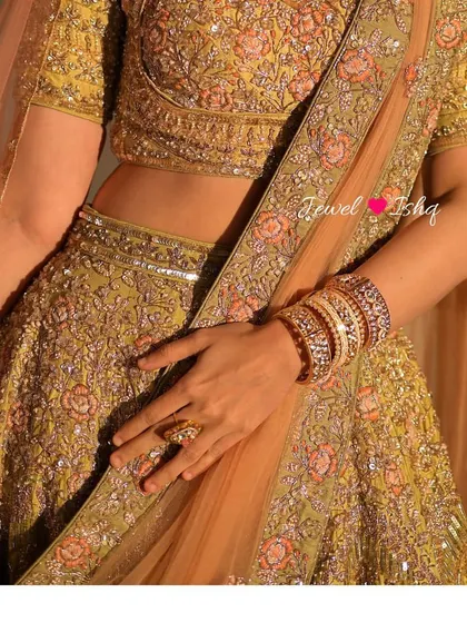 A detail shot of the bride's waist, showing her hand resting on her lehenga. The focus is on the beautiful stack of kadas and rings.