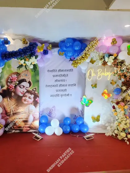 A traditional baby shower or naming ceremony setup with a Krishna-themed backdrop and an "Oh Baby" neon sign.