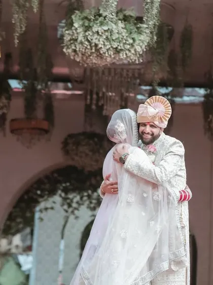 A heartfelt hug between the newly married couple. The grand decor of the venue provides a beautiful backdrop for this emotional moment.