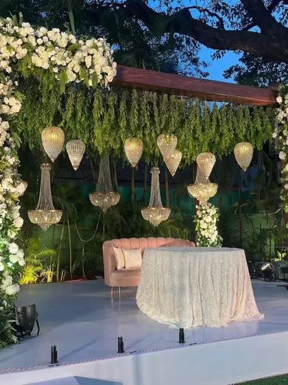 A close-up of a stage setup, showing the detail of the floral arch, hanging greenery, and elegant chandeliers.