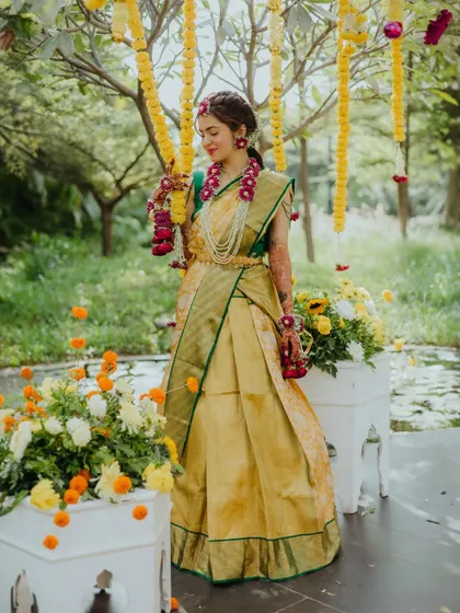 A full-length portrait of the bride, looking radiant in her Haldi attire, surrounded by marigold decorations.