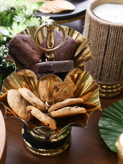 This two-tiered gold stand with scalloped edges is designed for serving sweets like brownies and cookies. Its polished finish and classic design bring a touch of timeless luxury to your high tea or dessert table.