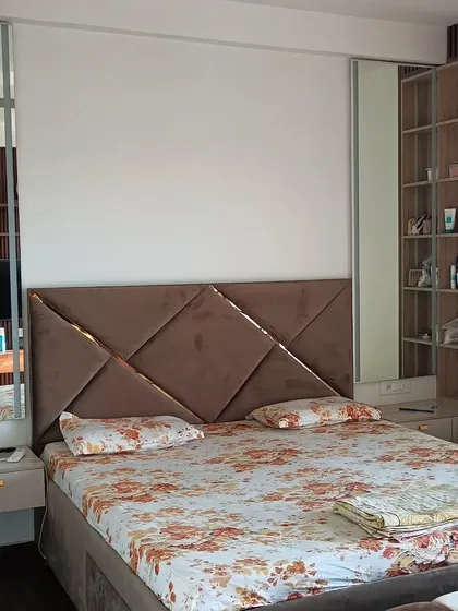 A customized bed with a unique geometric upholstered headboard. The design also includes backlit custom mirrors and wall-mounted side tables for a complete, integrated look.
