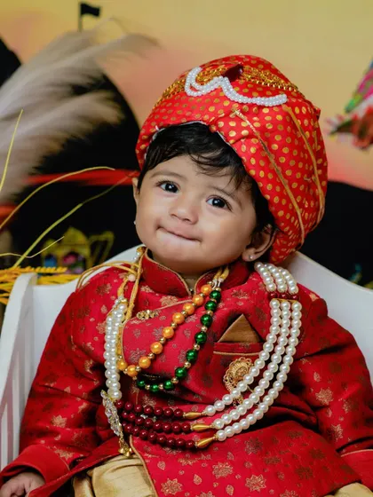 A smiling toddler in his red sherwani and turban.