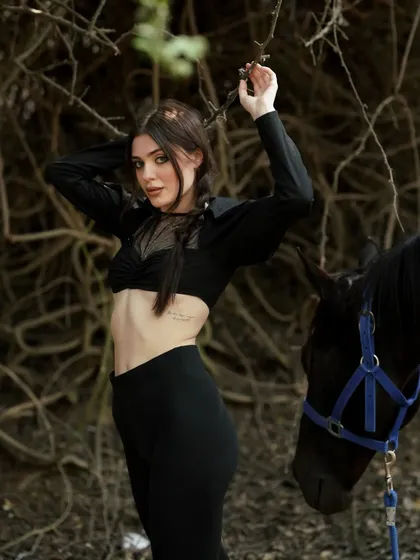 This image captures a moment of connection between the model and the dark horse, set against a natural, textured background.