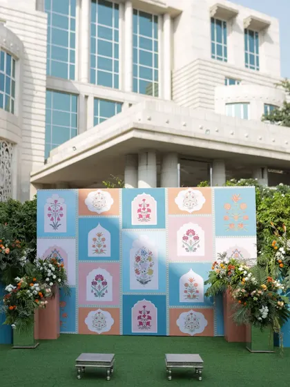 A beautiful pastel-colored backdrop with Mughal-inspired floral motifs, flanked by lush floral arrangements, perfect for a sophisticated Haldi or Mehendi.