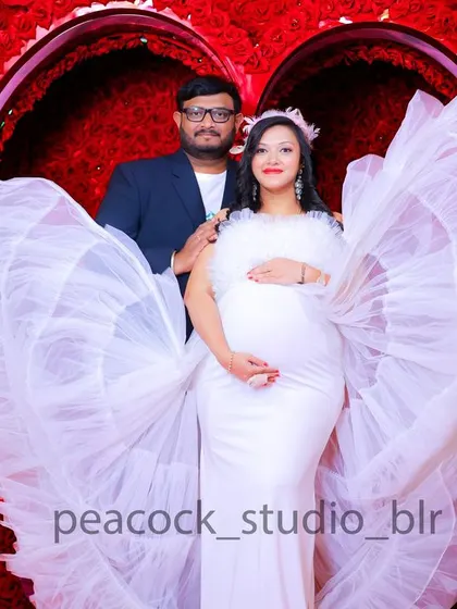 A beautiful couple's maternity photo. The expectant mother wears a white gown with angel-like wings, and her partner stands beside her in a sharp suit.