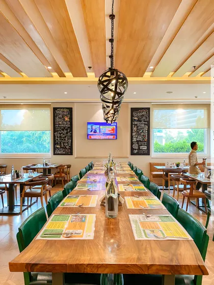 The long community table at Citrus Cafe, Bengaluru, is perfect for large groups or co-working. The design is anchored by striking pendant lights and a slatted wood ceiling detail.