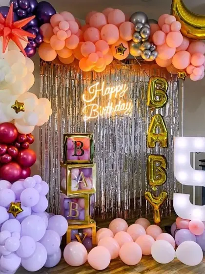 A colorful 5th birthday party setup with a silver shimmer backdrop, 'BABY' balloon boxes, and a large '5' marquee light.