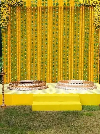 A simple yet elegant outdoor Haldi setup. The wall of marigold strings and the traditional brass urlis create a serene and beautiful space for the ceremony.