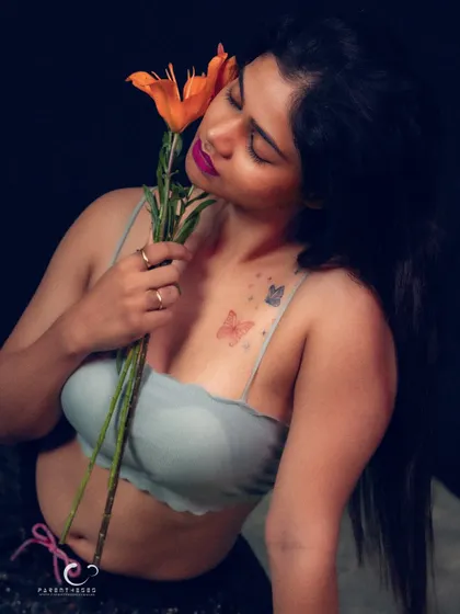 A soft and sensual portrait, with her eyes closed as she holds the flower to her cheek. The butterfly tattoo adds another layer of delicate beauty.