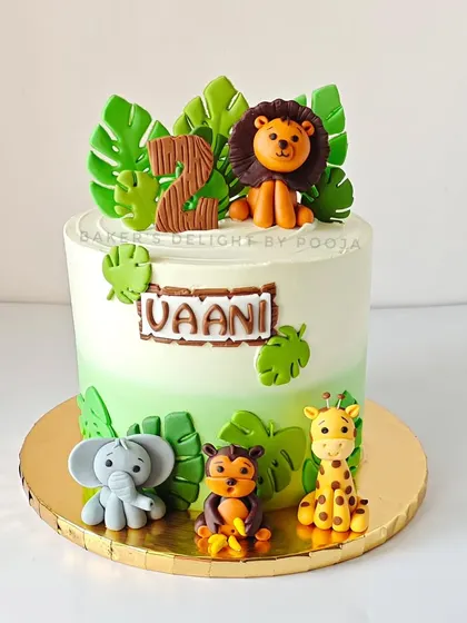 A full view of the elegant safari cake for Vaani's second birthday. The handcrafted fondant lion, elephant, monkey, and giraffe are set against a backdrop of lush, edible leaves for a chic jungle vibe.