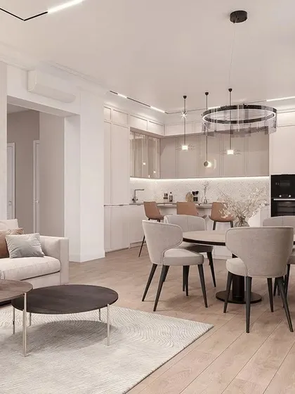 A wide view of an open-plan apartment where the living, dining, and kitchen areas flow into one another. The consistent use of light wood tones and a soft, neutral palette creates a sense of spaciousness and calm.