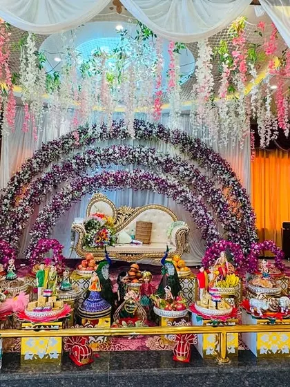 A luxurious platter display under a beautiful floral arch. The purple and white theme of the stage decor is reflected in the platter arrangements, creating a harmonious and rich look.