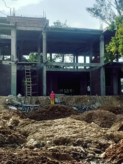 A wide view of the farmhouse construction site, showing the concrete frame and initial brickwork. The scale of the project is designed to be substantial yet respectful of the surrounding natural environment.