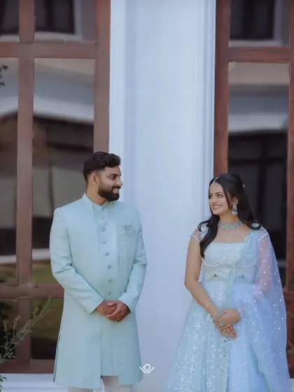 A lovely portrait of a couple in matching pastel blue outfits for their engagement, smiling at each other.