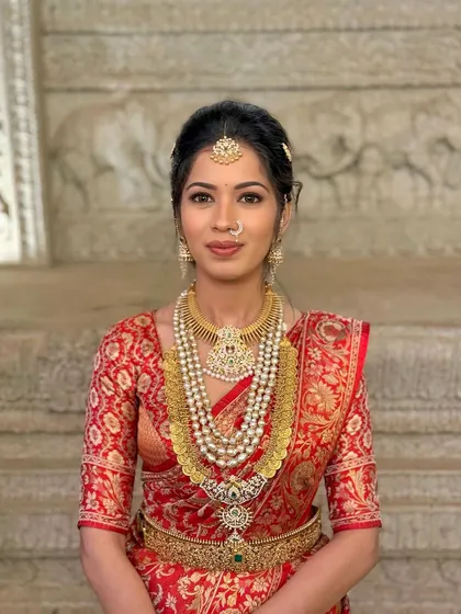 Embracing tradition with a bold twist. This radiant red saree look is enhanced with a skin-like finish, soft yet striking eye makeup, and traditional hair accessories like the Surya Chandra for a classic bridal look.