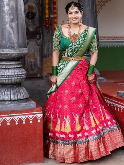 A full-length view of a client wearing a traditional red and green half saree. The skirt features unique motifs, adding a special touch to this classic ensemble.