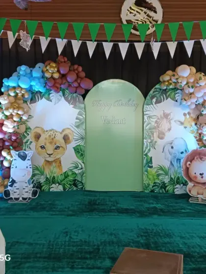 A stage setup for a jungle-themed party with cute baby animal cutouts and a white picket fence. The arched backdrops and balloon clusters create a lovely photo opportunity.