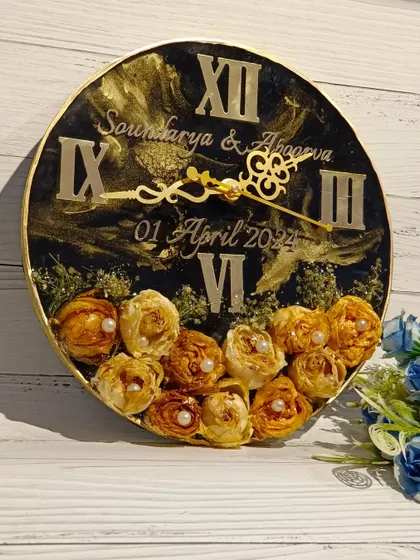 This black and gold preservation clock features a beautiful arrangement of preserved yellow roses at the bottom. The elegant script and classic Roman numerals make it a timeless piece.