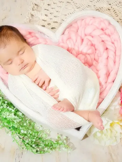 A newborn sleeps soundly in a heart-shaped basket, surrounded by soft greenery and flowers. This overhead shot is a beautiful composition of love and new life.