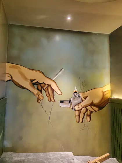 A modern twist on a classic, this mural in a pub's smoking area depicts the iconic hands from "The Creation of Adam," but this time, one is offering a light for a cigarette.