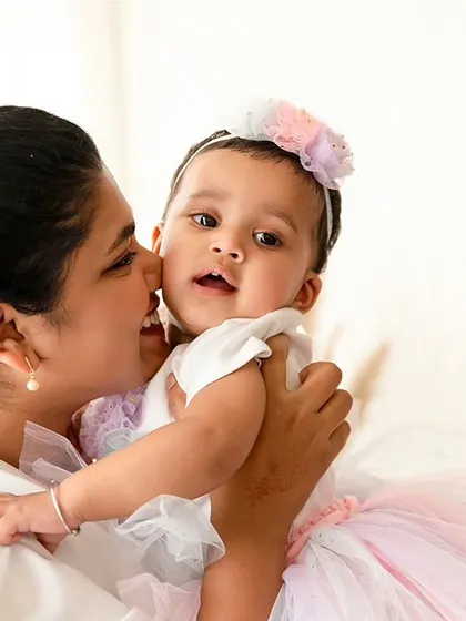 A mother holds her baby girl close, about to give her a kiss on the cheek.