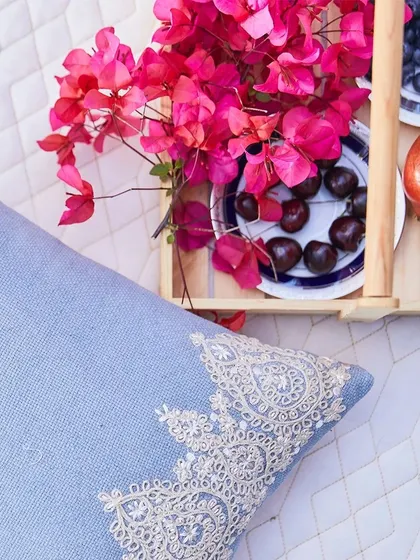 Let your home become a gallery of Indigo dreams. This beautiful flat-lay shows a light blue cushion with delicate white lace embroidery, paired with fresh fruits and flowers for a summery feel.