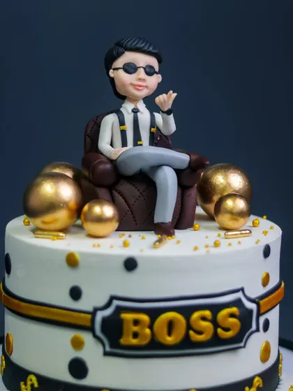 A close-up of the stylish "Boss" cake topper, a figurine of a man in a leather chair surrounded by gold spheres.