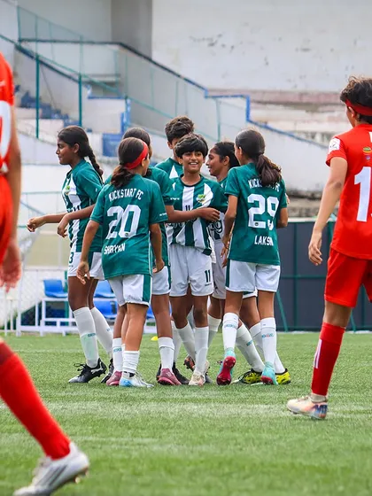 A moment of celebration and strategy as our U13 girls' team huddles up after scoring a goal against their opponents in red.
