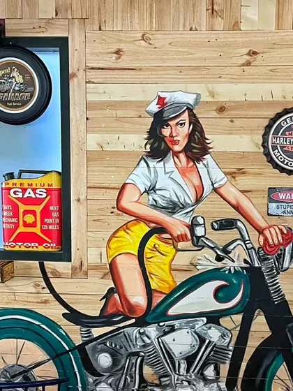 We created this retro pin-up style mural for Downtown Diner, featuring a woman washing a motorcycle. The artwork is painted on wooden panels and integrated with real objects to create a 3D effect.