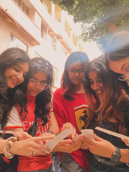 A group of friends gathered around, excitedly looking at their collection of photo strips.